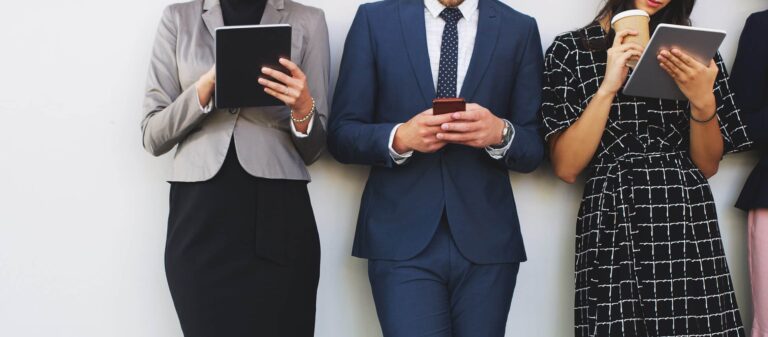 Drei Geschäftsleute stehen an einer Wand und haben ein Tablet oder Handy in der Hand