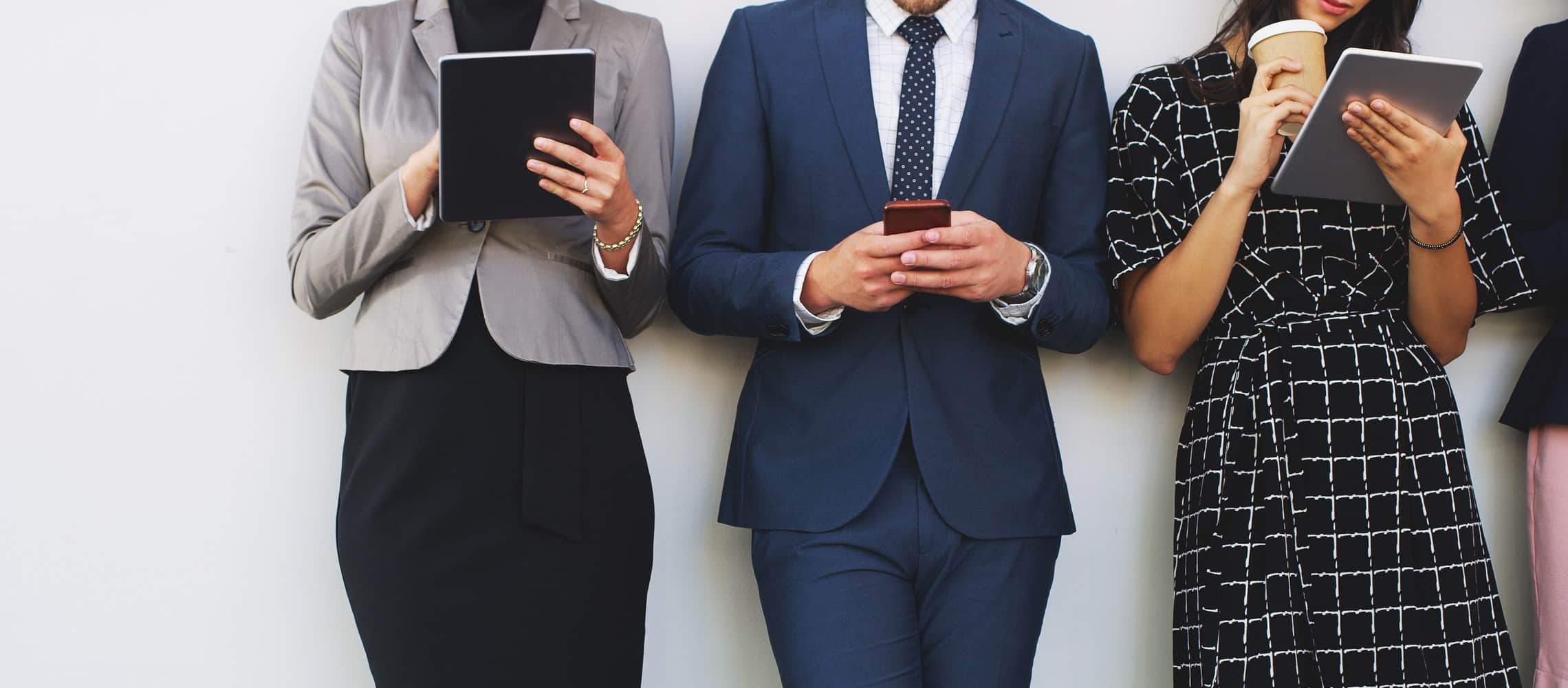 Drei Geschäftsleute stehen an einer Wand und haben ein Tablet oder Handy in der Hand