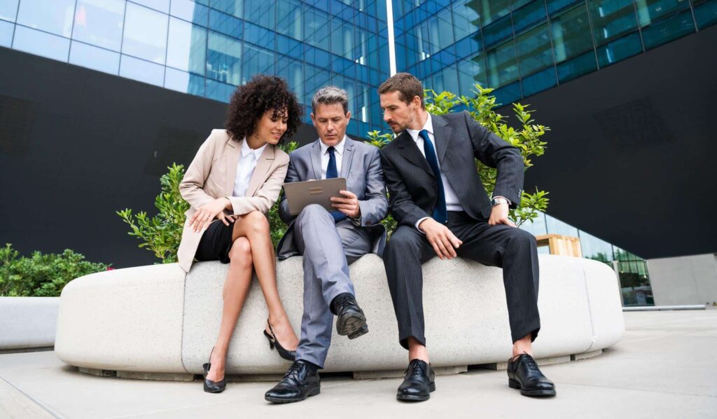 Social Media Recruiting, 3 Geschäftsleute sitzen vor einem Gebäude und schauen auf ein Tablet