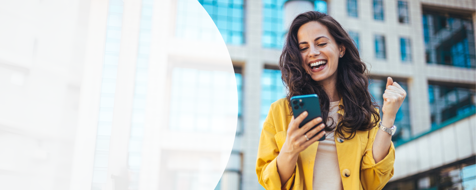 Frau mit langen brauen Haaren und gelber Jacke schaut voller Freude auf ihr Smartphone