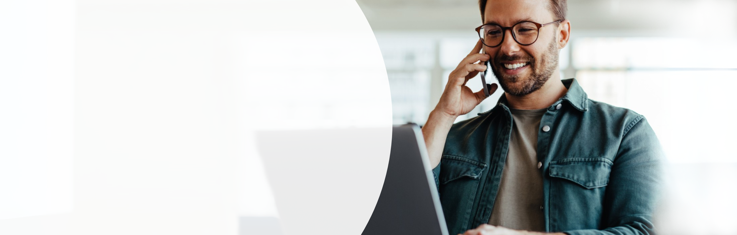 Mann mit Brille sitzt vor Laptop und telefoniert am Handy