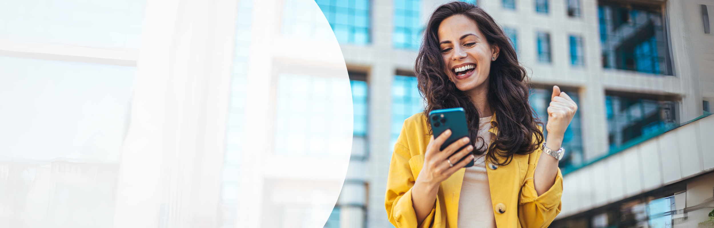 Frau mit langen brauen Haaren und gelber Jacke schaut voller Freude auf ihr Smartphone