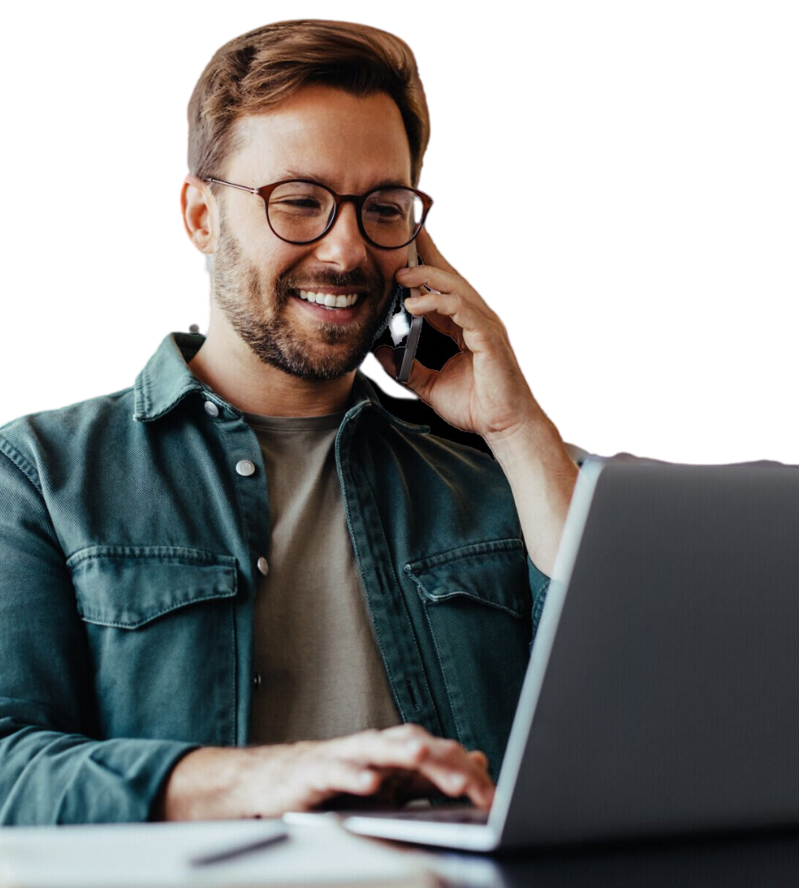 Ein Mann in einer blauen Jeansjacke telefoniert und sieht dabei in seinen Laptop.