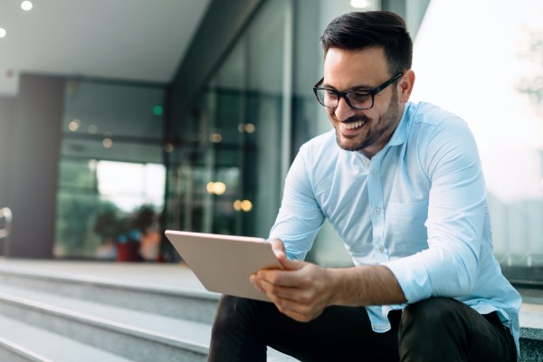 Mann mit hellblauem Hemd, Bart und Brille schaut lächelnd auf sein Tablet