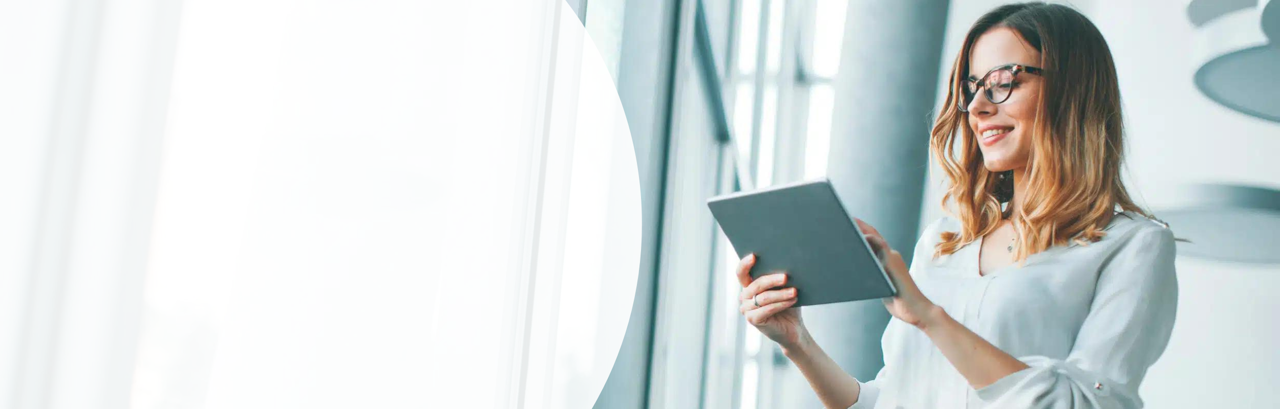 Lächelnde Frau in einer weißen Bluse sieht auf das Tablet, das sie in den Händen hält.