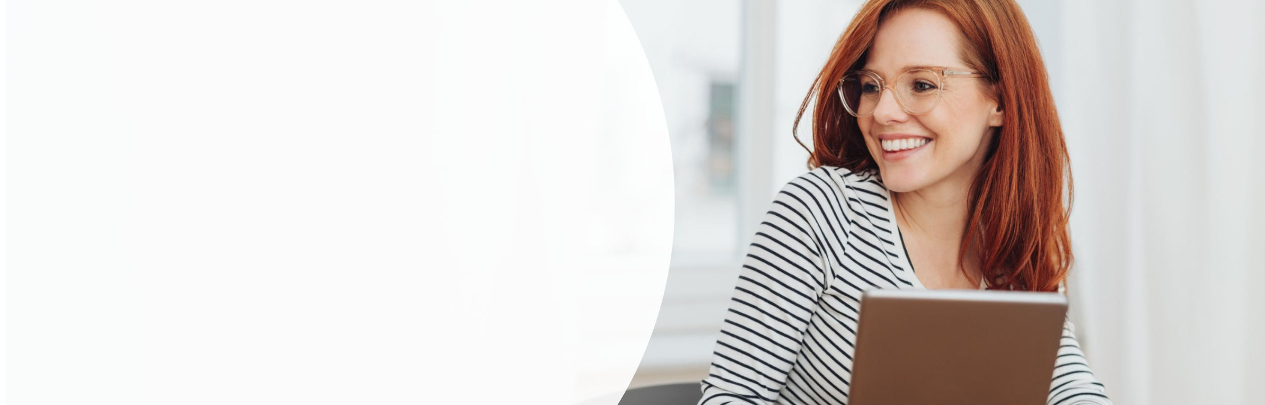 Frau mit rötlichen Haaren, gestreiftem Shirt und Brille sitzt am Tablet und lächelt