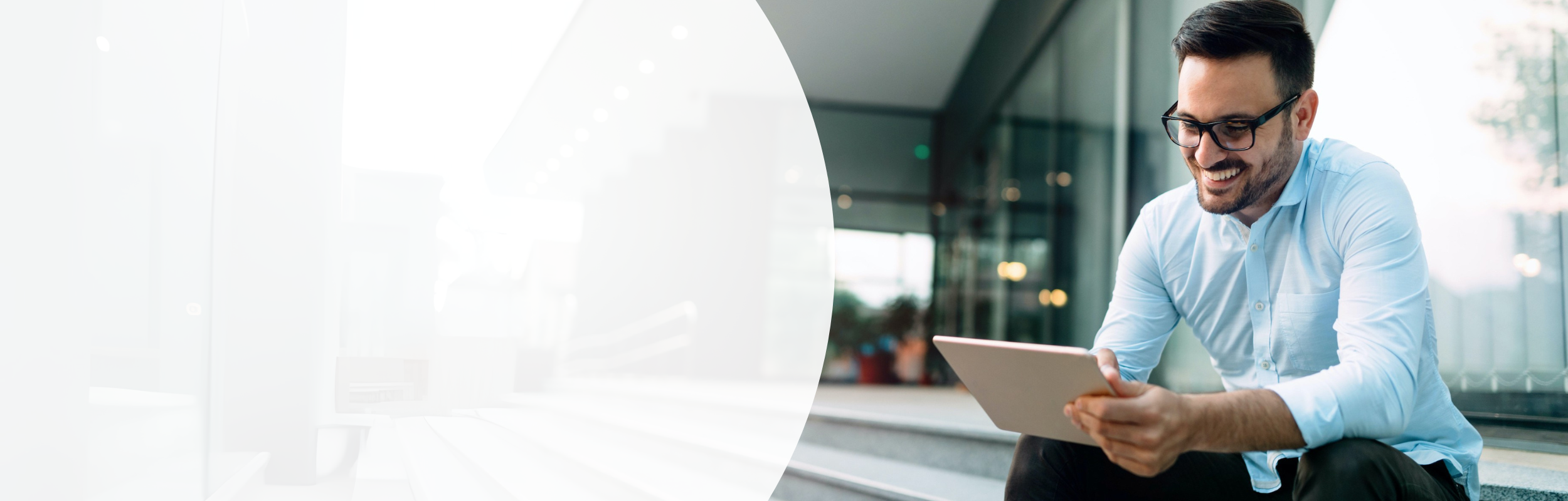 Mann mit hellblauem Hemd, Bart und Brille schaut lächelnd auf sein Tablet