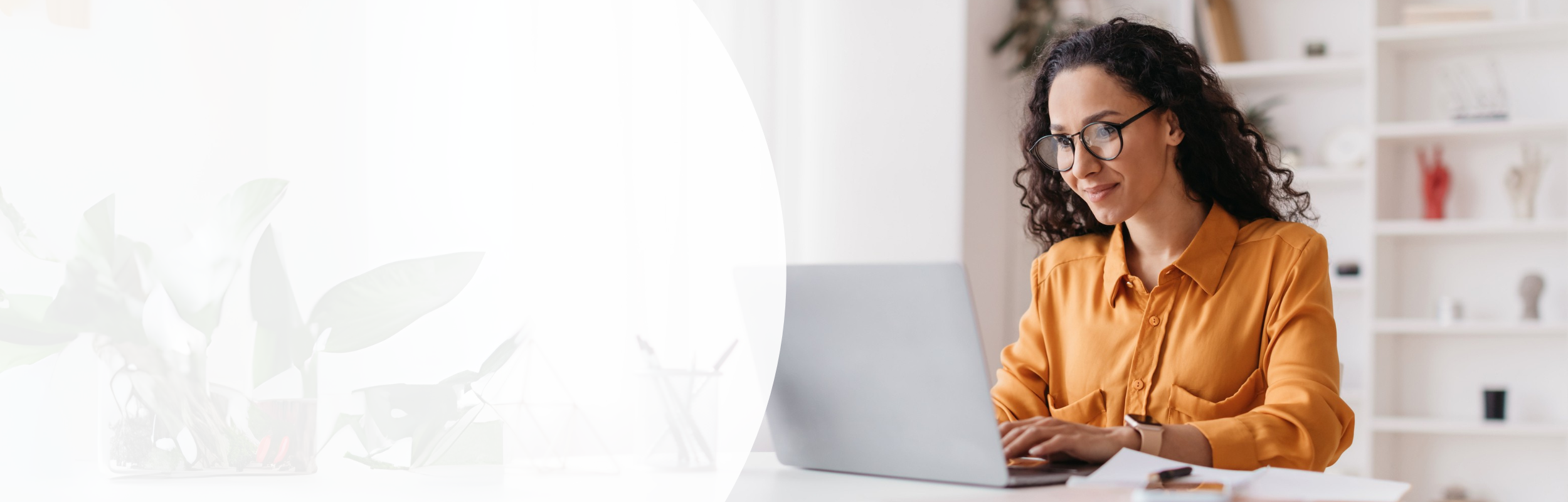 Frau mit langen gewellten Haaren, Brille und orangener Bluse sitzt vor Laptop
