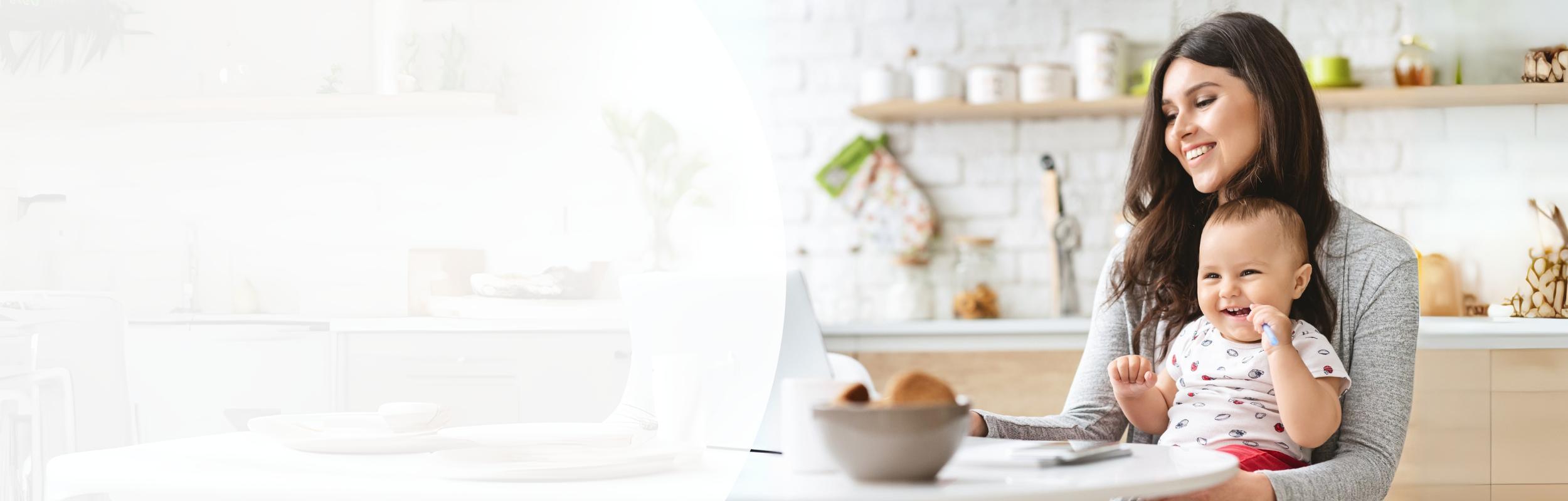 Frau mit langen braunen langen Haaren sitzt in der Küche mit Baby auf dem Schoss vor einem Laptop