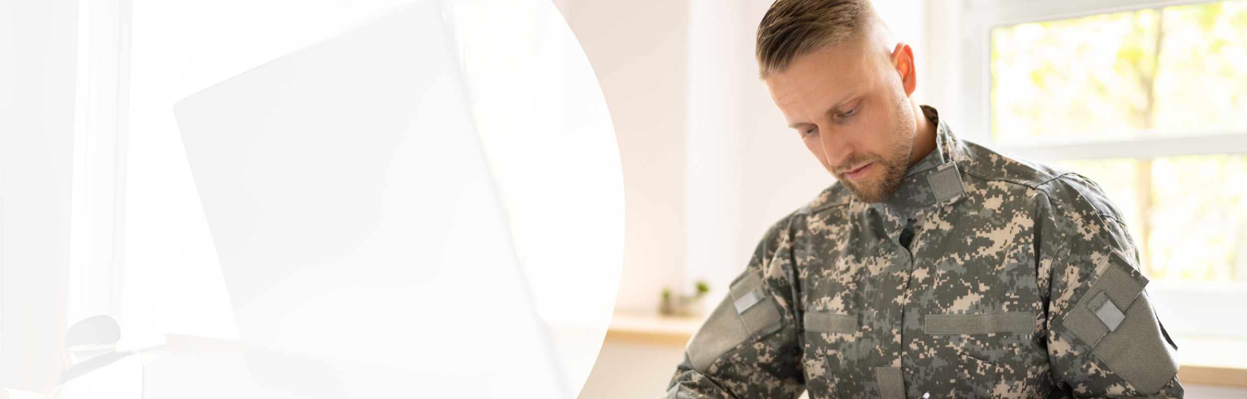 Ein Mann in Bundeswehr-Dienstkleidung sitzt an einem Schreibtisch und schreibt Notizen auf ein Klemmbrett, das vor ihm liegt.