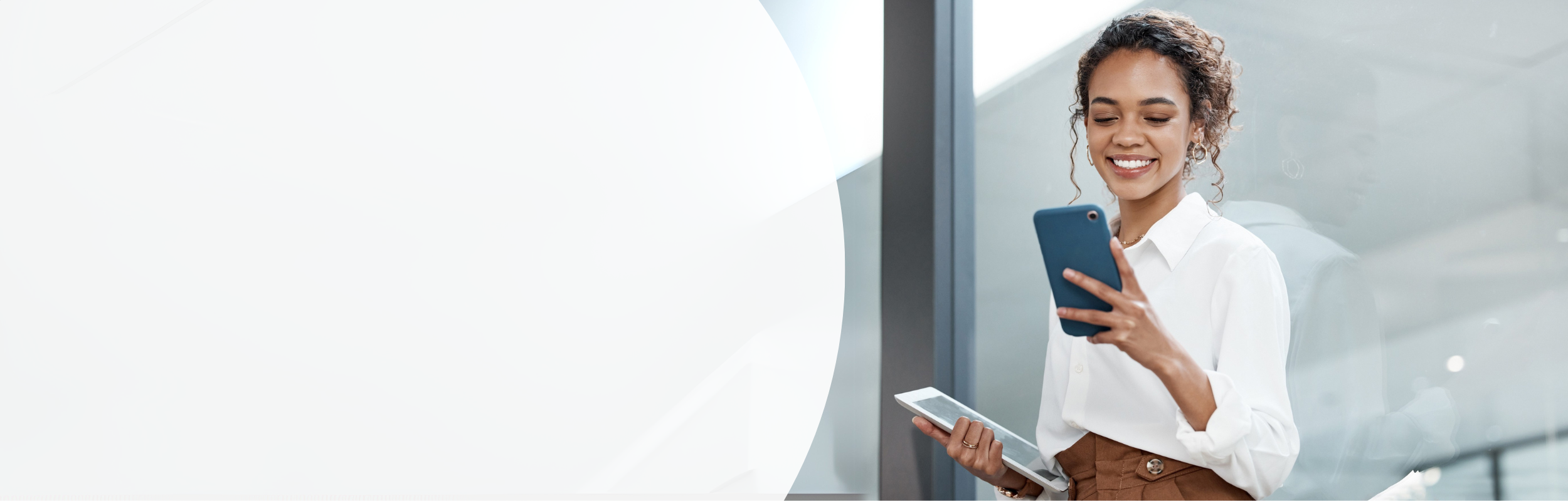 Frau mit Tablet in der einen Hand schaut lächelnd auf Smartphone