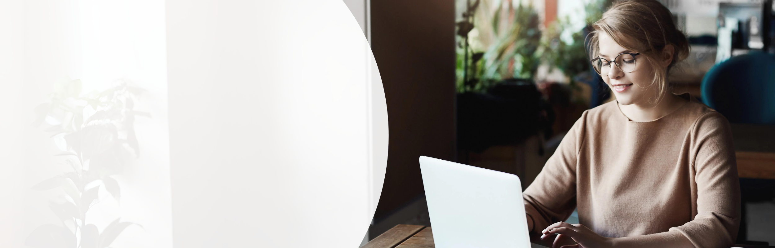 Junge Frau sitzt an einem Schreibtisch, vor ihr steht ein aufgeklappter Laptop.