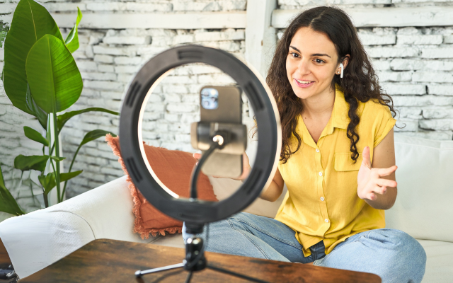 Frau mit langen brauen Haaren und gelber Jacke schaut voller Freude auf ihr Smartphone