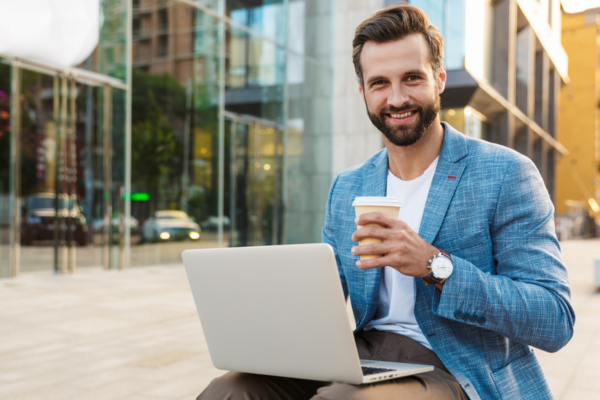 Ein Mann im blauen Jackett sitzt mit einem Becher Kaffee vor einem Laptop