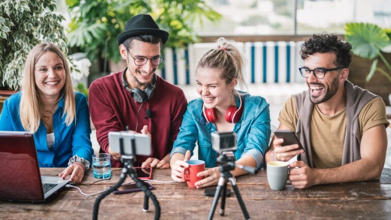 2 junge Frauen und zwei Männer sitzen an einem Tisch mit Laptop und Webcam