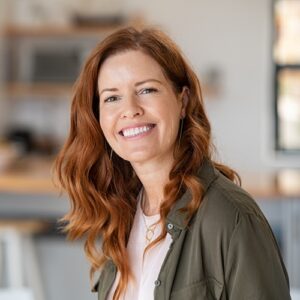 Lächelnde Frau mit langen rötlich gewellten Haaren.