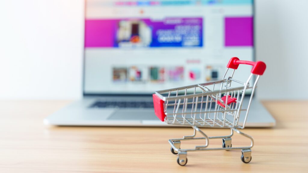 Miniatur Einkaufswagen steht vorderhalb eines aufgeklappten Laptops