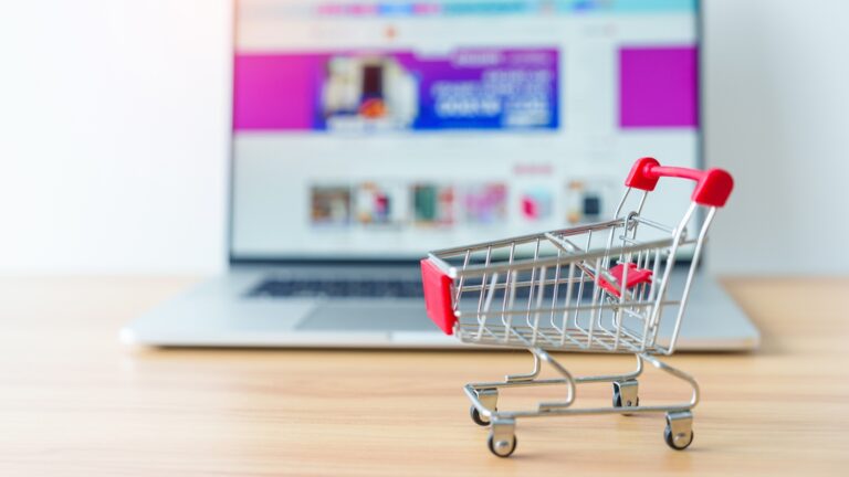 Miniatur Einkaufswagen steht vorderhalb eines aufgeklappten Laptops