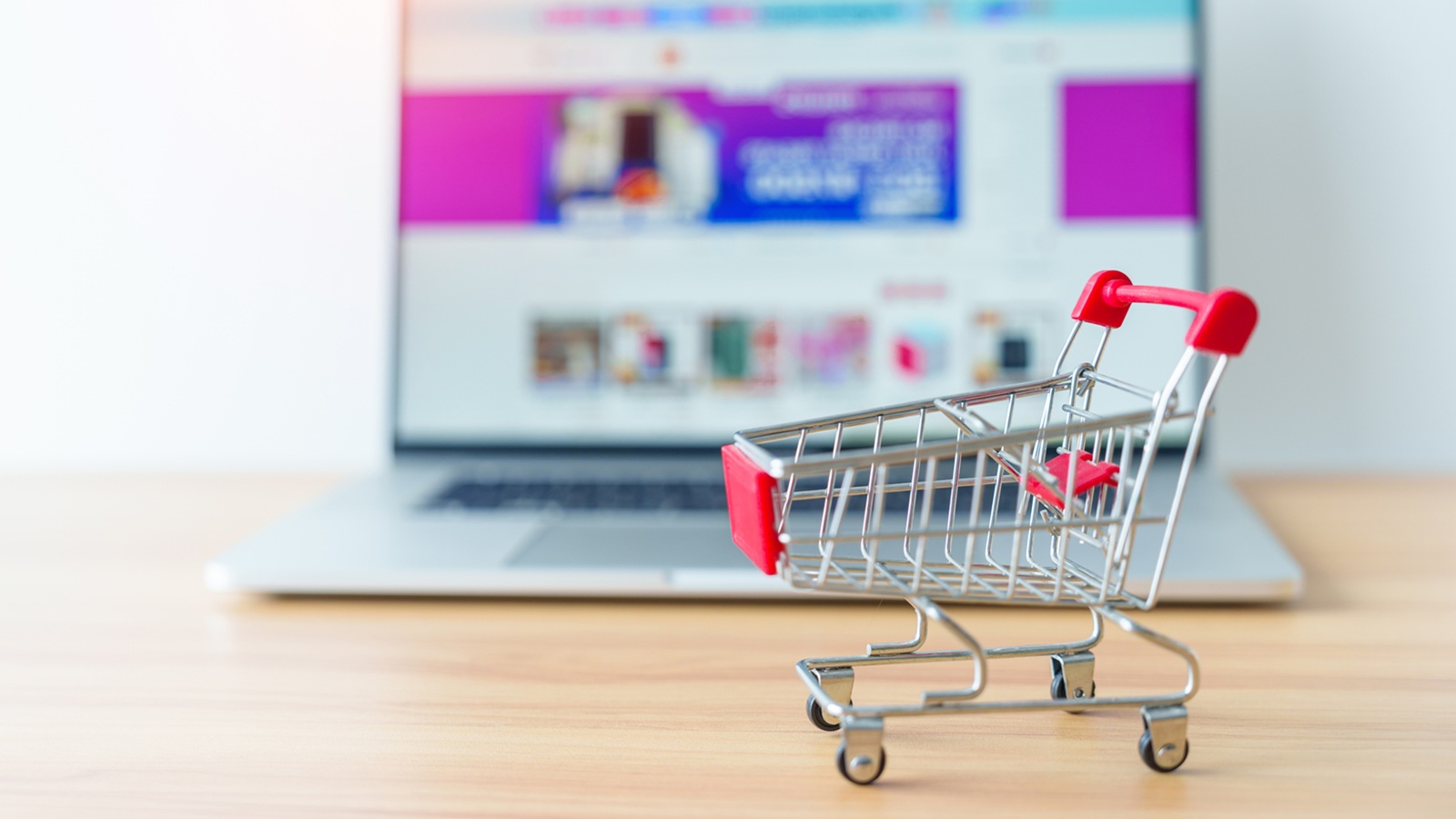 Miniatur Einkaufswagen steht vorderhalb eines aufgeklappten Laptops