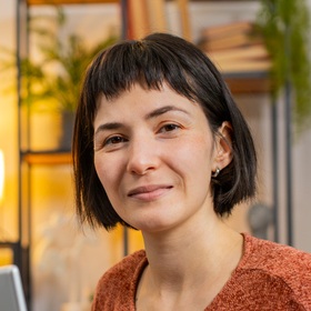 Portrait einer jungen Frau mit kurzen dunkelbraunen Haaren und einem orangenen Shirt.