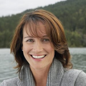 Portrait einer lächelnden Frau mit schulterlangem braunen Haar und einem grauen Pullover.