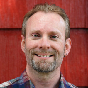 Portrait eines lächelnden Mannes mittleren Alters in einem karierten Hemd.