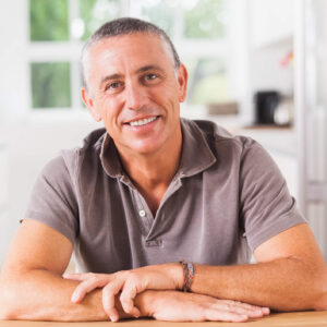 Portrait eines lächelnden Mannes mittleren Alters, der an einem Holztisch sitzt.